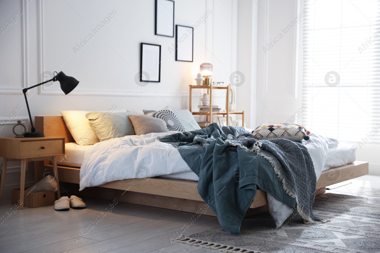 Cozy bed with soft linens, nightstand and lamp in stylish room. Home textile Photo of Cozy bed with soft linens, nightstand and lamp in stylish room. Home textile