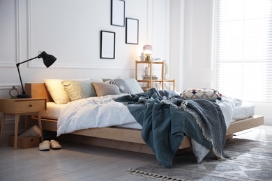Photo of Cozy bed with soft linens, nightstand and lamp in stylish room. Home textile