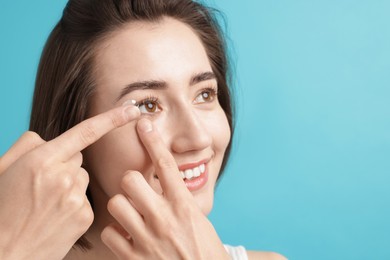 Photo of Woman putting in contact lens on light blue background. Space for text