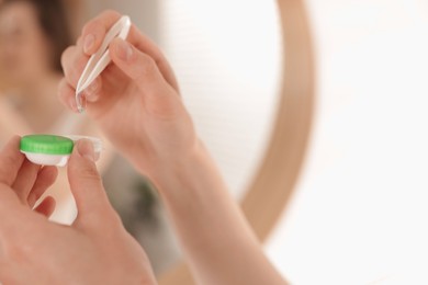 Photo of Woman taking contact lens out of case indoors, closeup. Space for text
