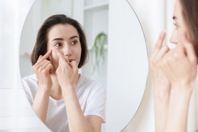 Photo of Woman putting in contact lens near mirror indoors