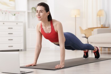Photo of Woman doing plank exercise during online class with coach at home. Sport and healthy lifestyle