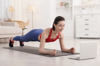 Photo of Woman doing plank exercise during online class with coach at home. Sport and healthy lifestyle