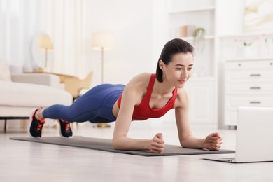 Photo of Woman doing plank exercise during online class with coach at home. Sport and healthy lifestyle