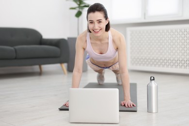 Photo of Woman doing plank exercise during online class with coach at home. Sport and healthy lifestyle