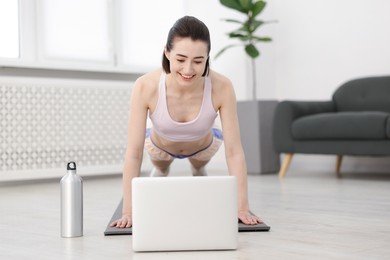 Photo of Woman doing plank exercise during online class with coach at home. Sport and healthy lifestyle
