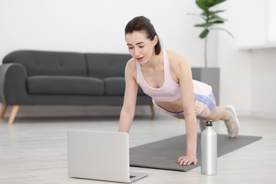 Photo of Woman doing plank exercise during online class with coach at home. Sport and healthy lifestyle