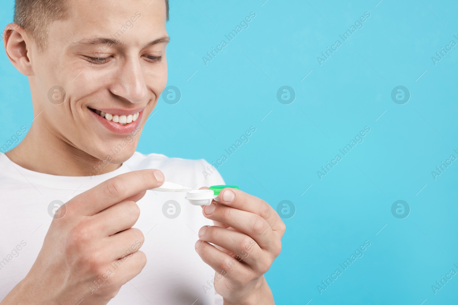Man taking contact lens out of case on light blue background, closeup. Space for text Photo of Man taking contact lens out of case on light blue background, closeup. Space for text