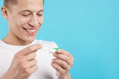 Photo of Man taking contact lens out of case on light blue background, closeup. Space for text
