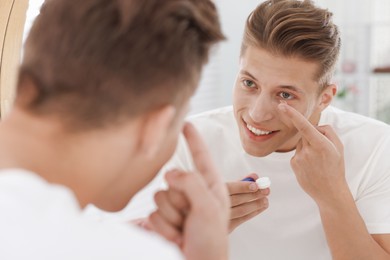 Photo of Man putting in contact lens near mirror at home