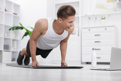 Photo of Man doing plank exercise during online class with coach at home. Sport and healthy lifestyle