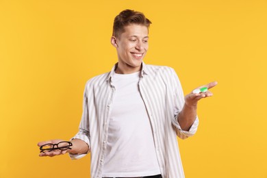Photo of Man choosing between glasses and contact lenses on yellow background