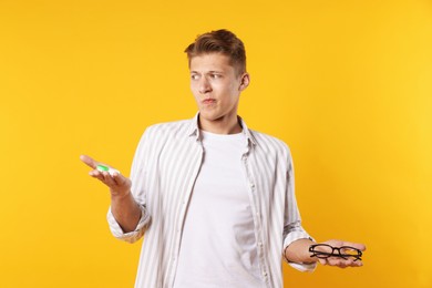 Photo of Man choosing between glasses and contact lenses on yellow background