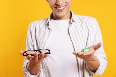 Photo of Man choosing between glasses and contact lenses on yellow background, closeup