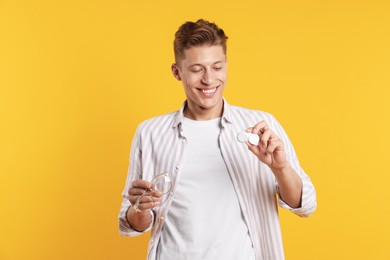 Photo of Man choosing between glasses and contact lenses on yellow background
