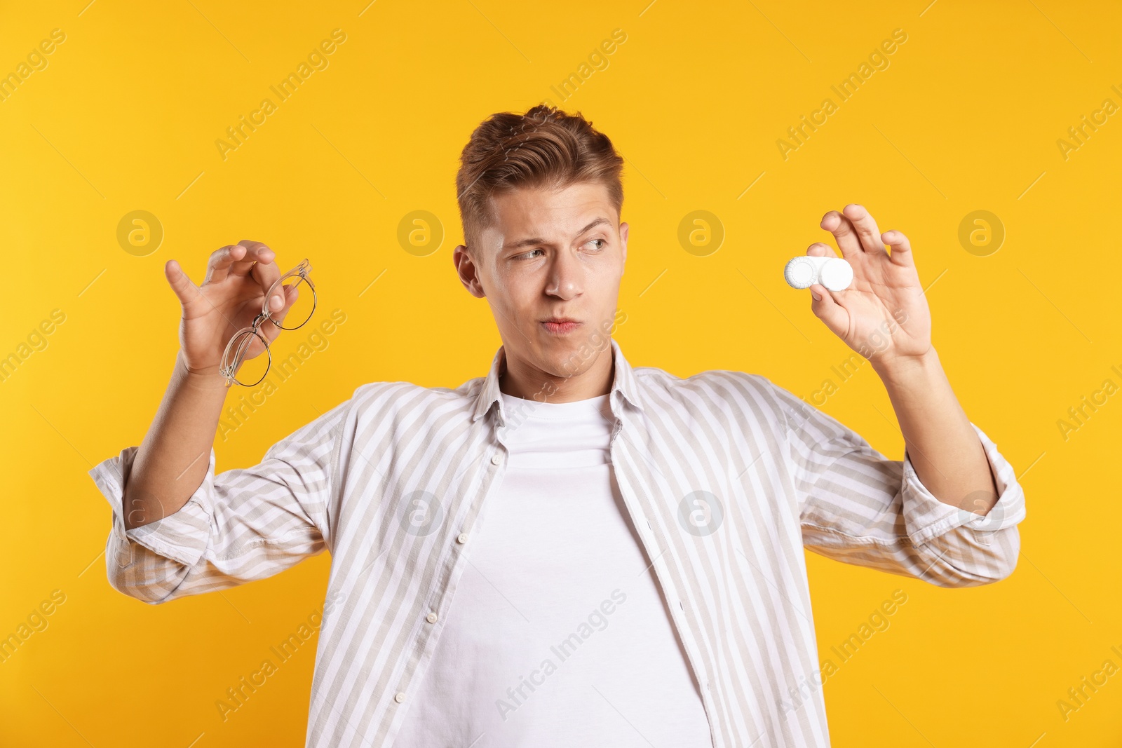 Man choosing between glasses and contact lenses on yellow background Photo of Man choosing between glasses and contact lenses on yellow background