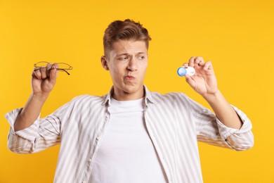 Photo of Man choosing between glasses and contact lenses on yellow background
