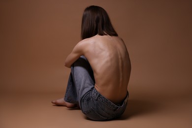 Photo of Woman suffering from anorexia on dark beige background, back view