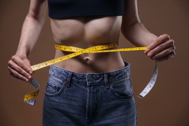 Photo of Anorexic woman measuring her waist on brown background, closeup