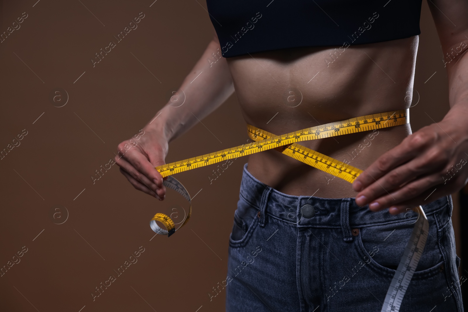 Anorexic woman measuring her waist on brown background, closeup Photo of Anorexic woman measuring her waist on brown background, closeup