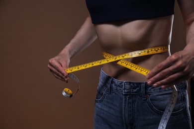 Photo of Anorexic woman measuring her waist on brown background, closeup