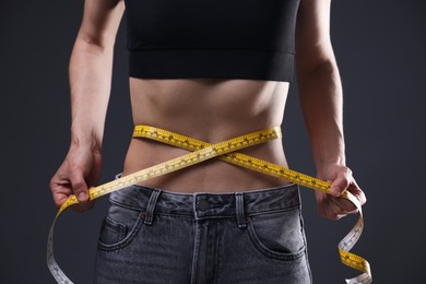 Photo of Anorexic woman measuring her waist on grey background, closeup