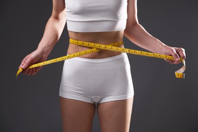 Photo of Anorexic woman measuring her waist on grey background, closeup