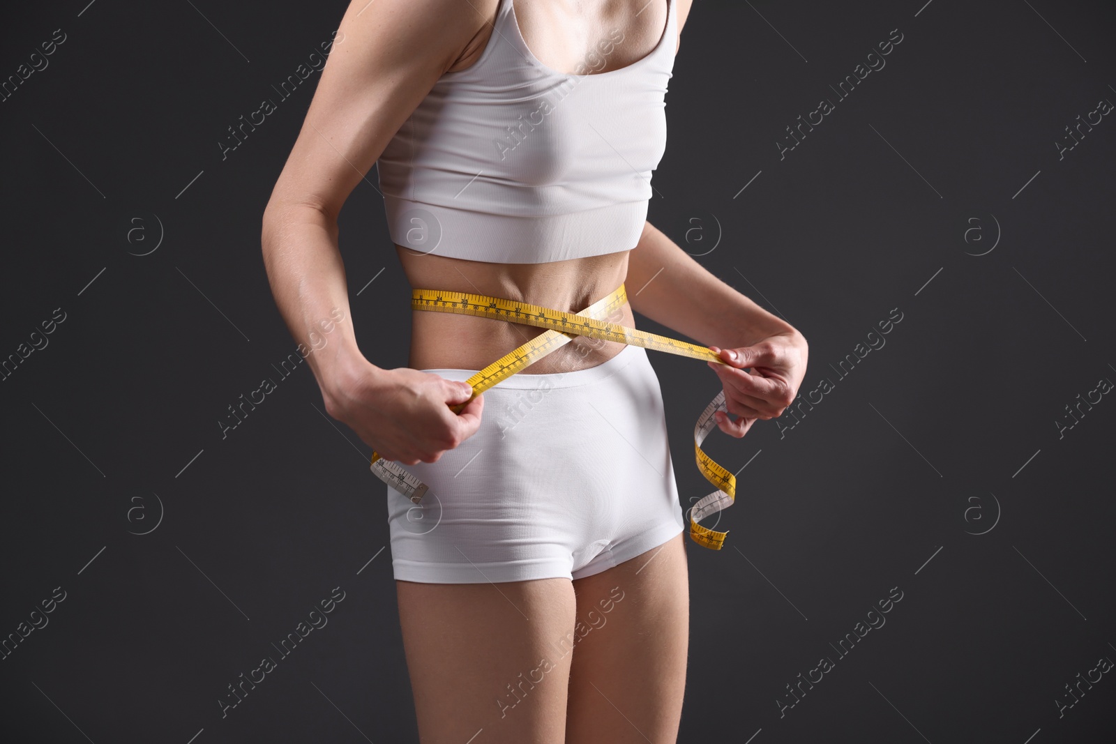 Anorexic woman measuring her waist on grey background, closeup Photo of Anorexic woman measuring her waist on grey background, closeup