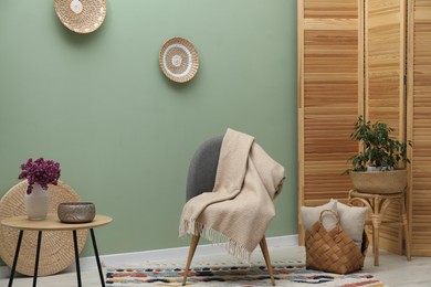 Photo of Comfortable armchair with woolen blanket, pillows and decor indoors
