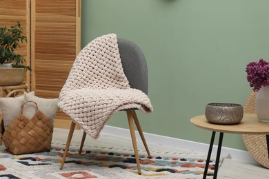Photo of Comfortable armchair with woolen blanket, pillows and decor indoors