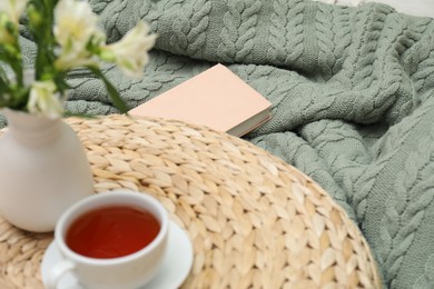Photo of Woolen blanket, book, tea and flowers indoors, closeup