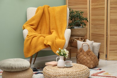 Photo of Comfortable armchair with woolen blanket, pillows and decor indoors