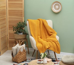 Photo of Comfortable armchair with woolen blanket, pillows and decor indoors