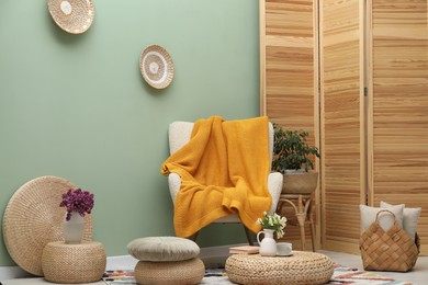 Photo of Comfortable armchair with woolen blanket, pillows and decor indoors