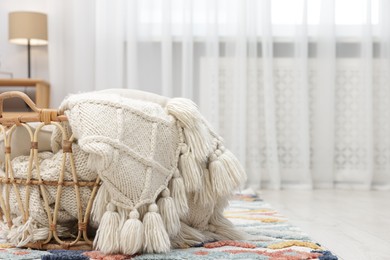 Photo of Woolen blanket in basket on floor indoors, space for text