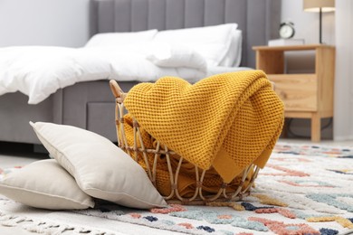 Photo of Woolen blanket in basket and pillows on floor indoors