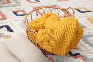 Photo of Woolen blanket in basket and pillows on floor indoors, closeup