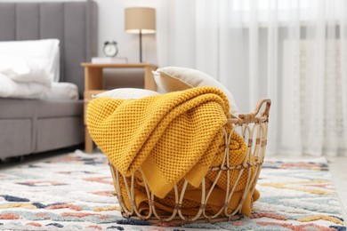 Photo of Woolen blanket and pillows in basket on floor indoors