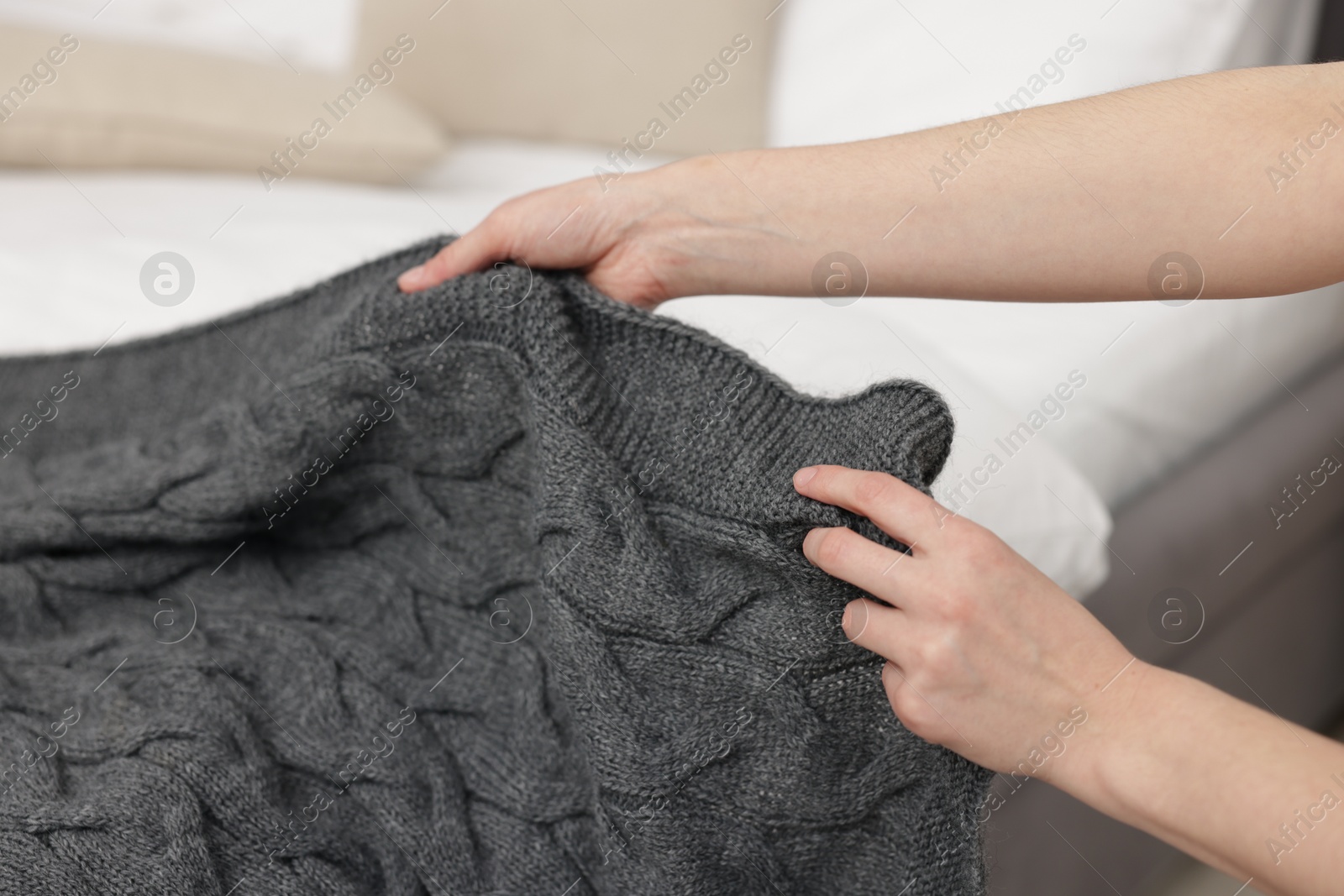 Woman putting woolen blanket on bed indoors, closeup Photo of Woman putting woolen blanket on bed indoors, closeup