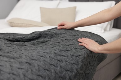 Photo of Woman putting woolen blanket on bed indoors, closeup