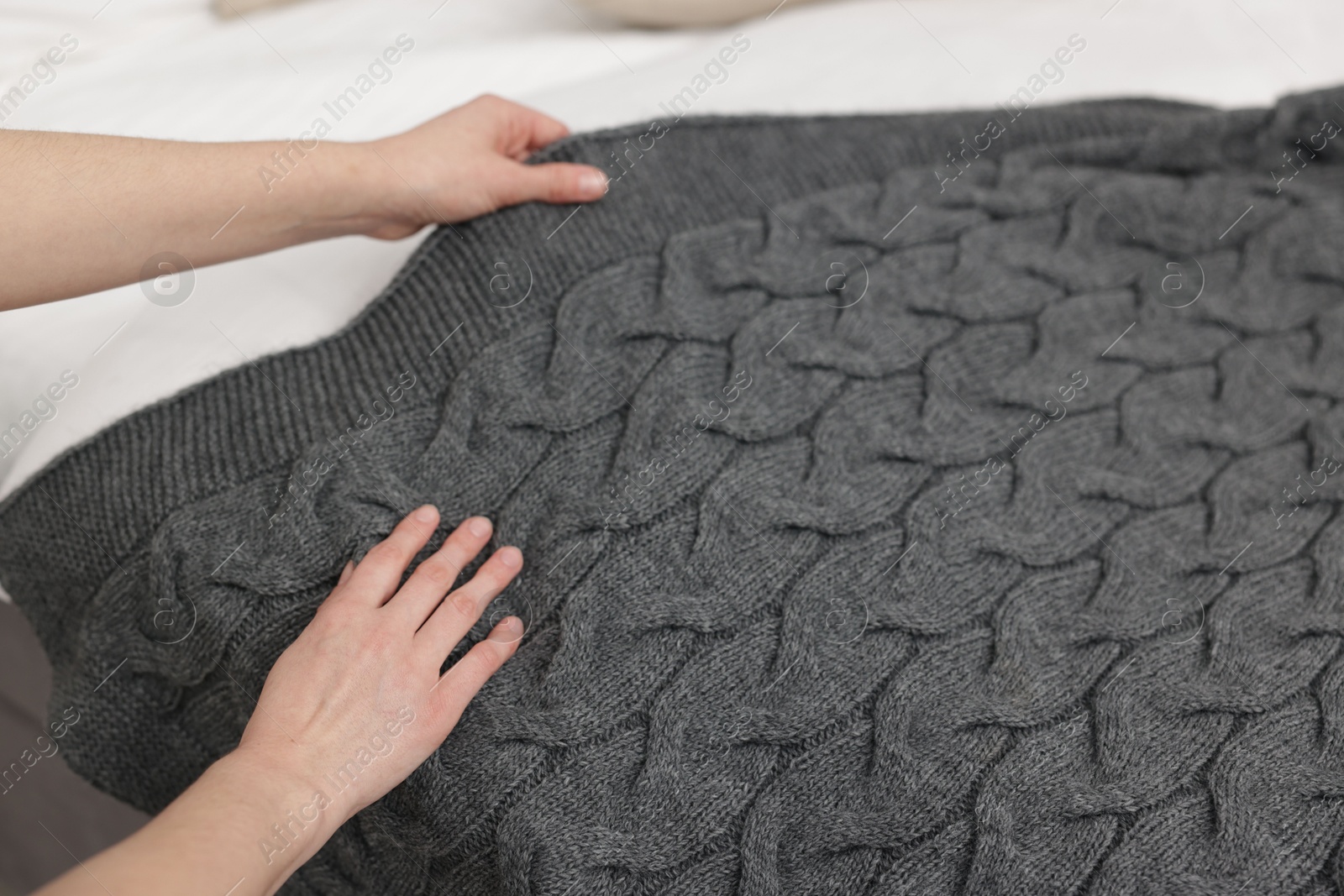 Woman putting woolen blanket on bed indoors, closeup Photo of Woman putting woolen blanket on bed indoors, closeup