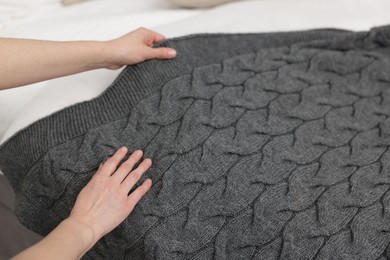 Photo of Woman putting woolen blanket on bed indoors, closeup