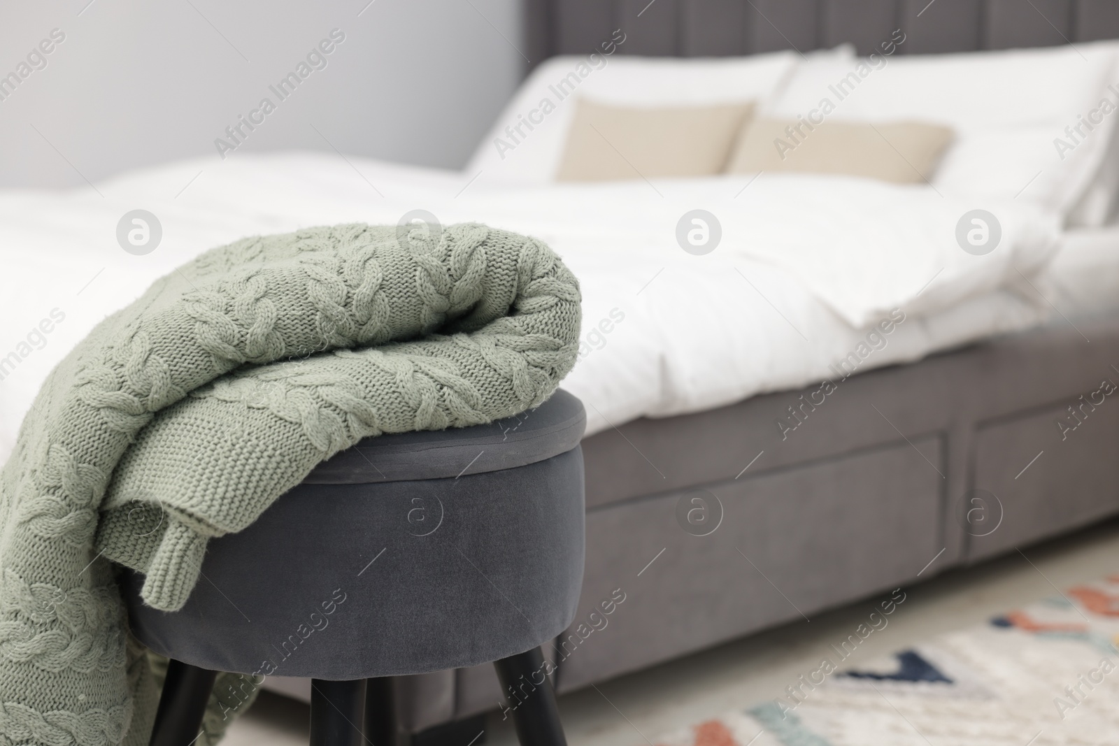 Woolen blanket on pouf indoors, space for text Photo of Woolen blanket on pouf indoors, space for text