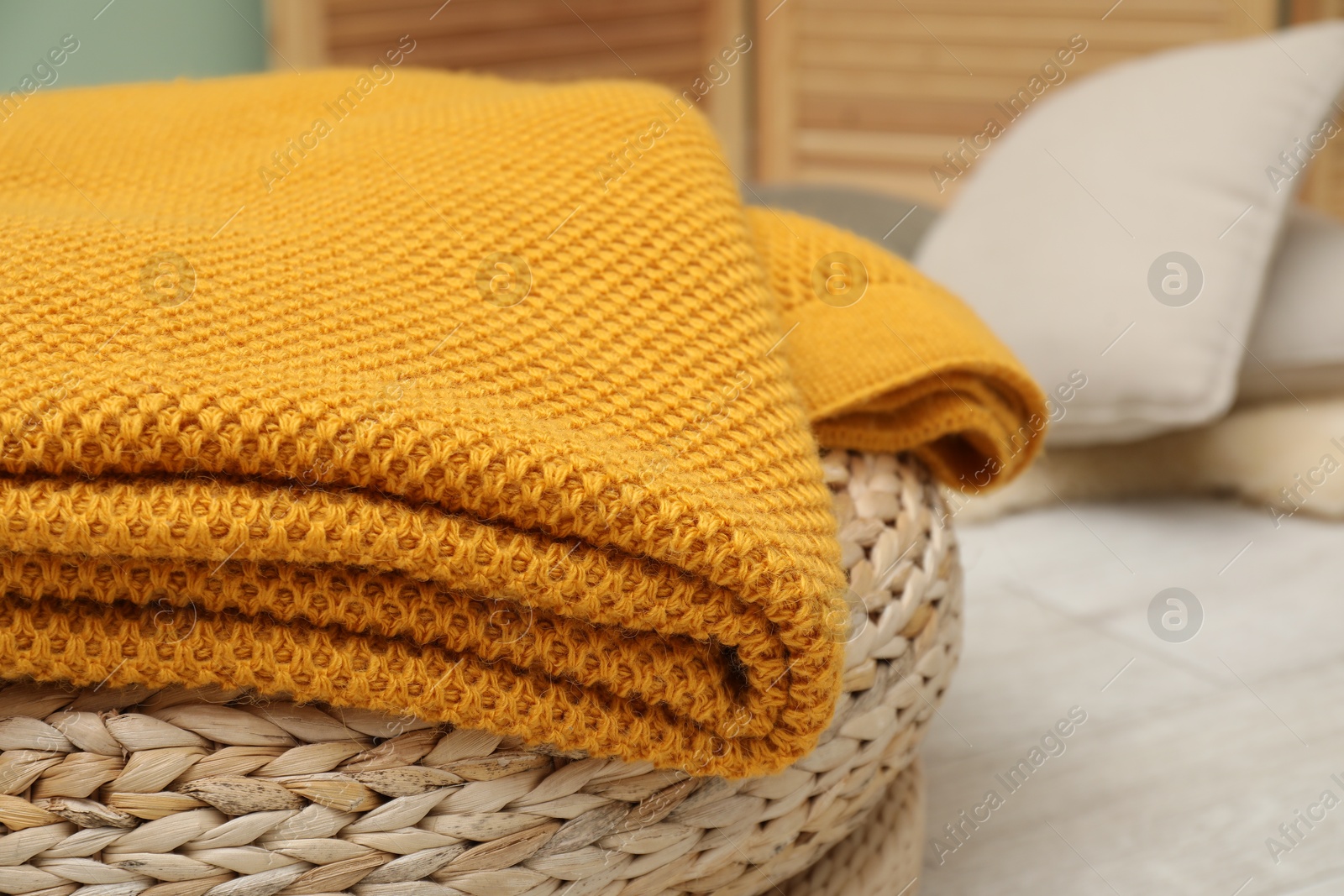 Woolen blanket near on pouf indoors, closeup. Space for text Photo of Woolen blanket near on pouf indoors, closeup. Space for text
