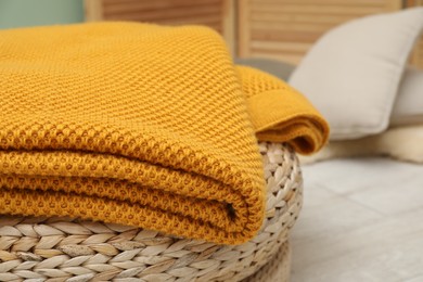 Photo of Woolen blanket near on pouf indoors, closeup. Space for text