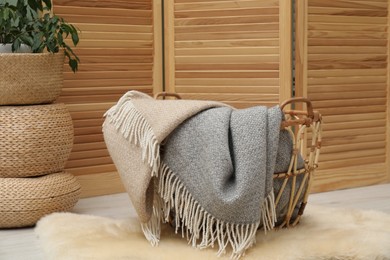 Photo of Woolen blankets in basket on floor indoors