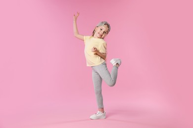 Photo of Cute little girl dancing on pink background