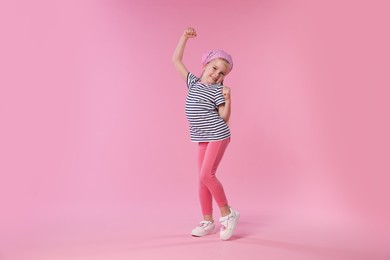 Photo of Cute little girl dancing on pink background