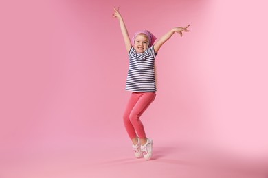 Photo of Cute little girl dancing on pink background