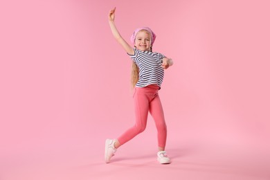 Photo of Cute little girl dancing on pink background